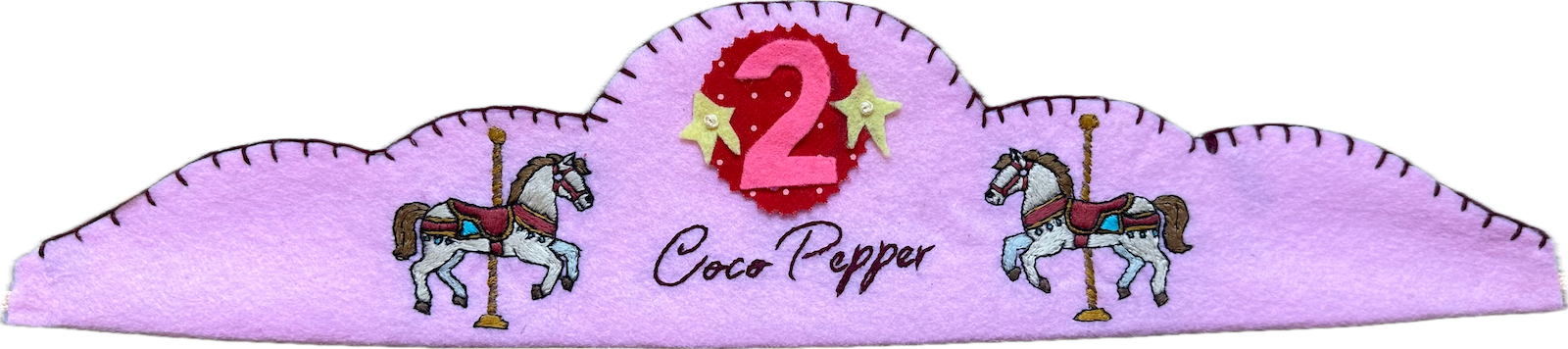 Lilac felt crown with two embroidered carousel horses, the name Coco Pepper in script, and a pink number 2 on a red polka-dot patch with yellow stars.