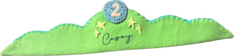 Lime-green felt crown with turquoise blanket stitching, yellow felt stars, the name Casey embroidered in navy script, and a blue sequined number 2 patch on top.