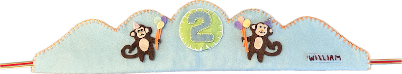 Pale-blue felt crown with two brown felt monkeys in party hats holding balloons, a green number 2 patch in the middle, and the name William stitched on a small label.